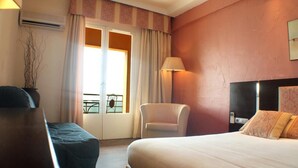 A hotel room with a bed, a chair, a desk, and a window with curtains. - Cavaliere Sur Plage (Le Lavandou)