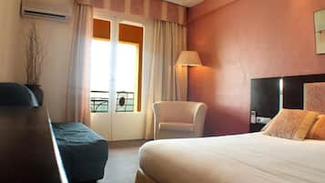 A hotel room with a bed, a chair, a desk, and a window with curtains.