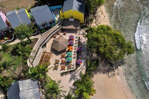 A beachfront property with multiple buildings, a patio area with umbrellas, and a sandy beach. - Crystal Cove by Elegant Hotels - All-inclusive (Derricks)