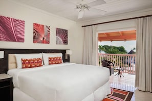A hotel room with a large bed, a ceiling fan, artwork on the wall, and a balcony with a view. - Crystal Cove by Elegant Hotels - All-inclusive (Derricks)