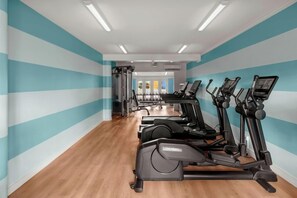 Un gimnasio con equipo de ejercicio, incluyendo cintas de correr y bicicletas estáticas, y piso de madera.