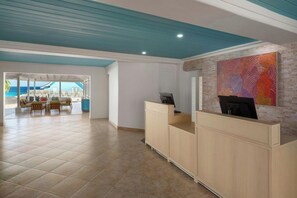 Zona de recepción de un hotel con vista al mar, un mostrador de recepción y un cuadro abstracto colorido en la pared.