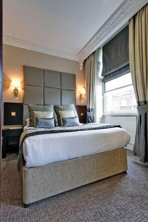 Ein Hotelzimmer mit einem großen Bett, zwei Nachttischen, einer Kopfteil und einem Fenster mit Vorhängen.