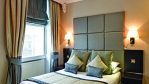 Ein Hotelzimmer mit einem großen Bett, zwei Nachttischlampen und einem fensterbelaubten Fenster.