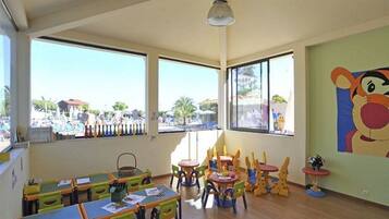 A classroom with large windows, colorful furniture, and a mural on the wall.