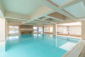 Une piscine intérieure aux murs en pierre, dotée de grandes fenêtres et d’un plafond haut.