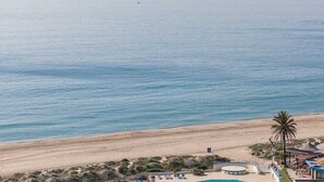 Vista de una playa con piscina, palmeras y un acantilado lejano.