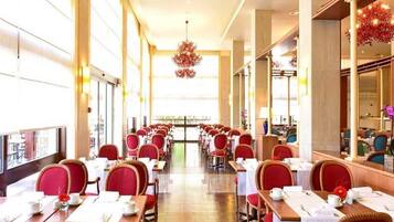 Un restaurante con mesas largas y sillas rojas, ventanas amplias y un candelabro.
