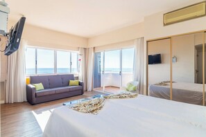 Habitación de hotel con cama, sofá, televisión y balcón con vista al mar.
