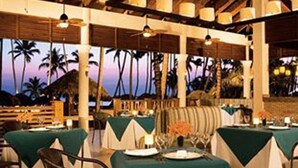 An outdoor dining area with tables set for two, covered with green tablecloths, and a wooden ceiling structure. - Jewel Palm Beach Resort Spa (Punta Cana)