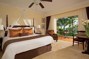 A hotel room with a four-poster bed, a ceiling fan, a view of the outdoors, a dining area, and a large window. - Dreams Palm Beach (Punta Cana)