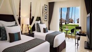 A hotel room with two beds, a ceiling fan, a TV, and a balcony with a view of palm trees and a pool. - Jewel Palm Beach Resort Spa (Punta Cana)