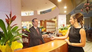Una mesa de recepción con un hombre y una mujer, una barra de madera y plantas en macetas.