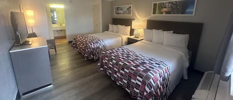 Ein Hotelzimmer mit zwei Betten, einem Schreibtisch, einem Kühlschrank und einem durch eine offene Tür einsehbaren Badezimmer.