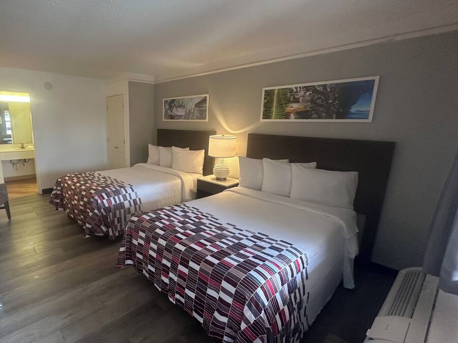 A hotel room with two beds, a desk, a refrigerator, and a bathroom visible through an open door.