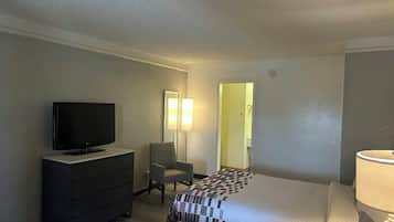 A hotel room with a bed, a television on a dresser, a chair, a lamp, and a door leading to another room.