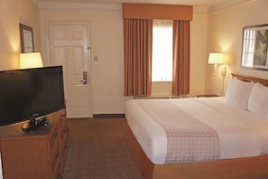 A hotel room with a bed, a television on a wooden cabinet, a door, and a window with curtains. - Baymont by Wyndham San Antonio South Park (San Antonio)