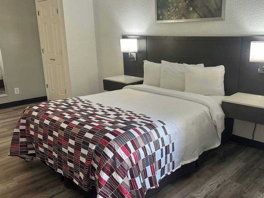 Hotelkamer met een bed, twee nachtkastjes, een wandlamp en een ventilatieopening.