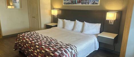 Ein Hotelzimmer mit einem großen Bett, zwei Nachttischen, einer Kopfteil und einem Wandbild sowie einer Tür.