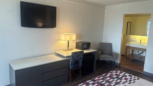 A compact room with a flat-screen TV, a desk with a lamp, a microwave, a chair, and a small bathroom with a sink and mirror. - Red Roof Inn San Antonio - South Park (San Antonio)