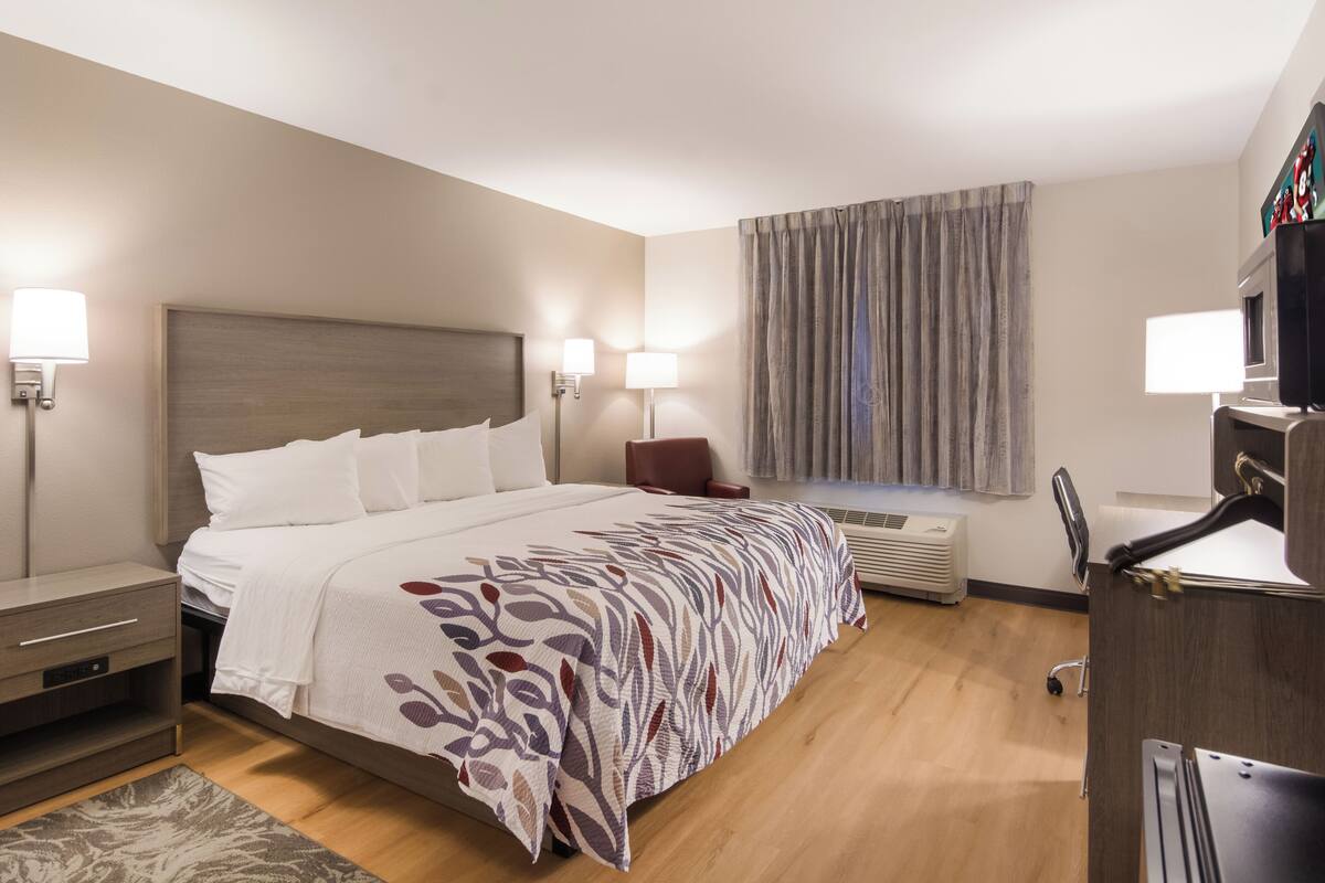 Une chambre d’hôtel comprenant un lit, des tables de chevet, un bureau, une chaise, une fenêtre avec des rideaux et un appareil de climatisation.
