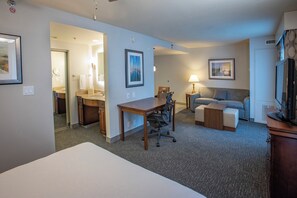 Ein Hotelzimmer mit Bett, Schreibtisch, Stuhl, Sofa, Fernseher und einem durch eine offene Tür einsehbaren Badezimmer.