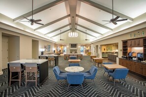 Un hall d’hôtel avec un plafond haut, des lustres, des ventilateurs de plafond, un espace salon central et un coin cuisine.
