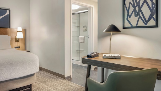 Una habitación de hotel con una cama, un escritorio, una silla, una lámpara, un teléfono y una obra de arte abstracta enmarcada en la pared.