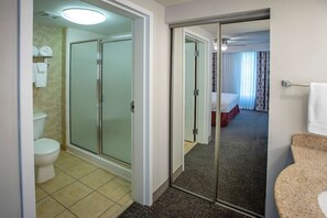 Ein Hotelbad mit Dusche, Toilette und einem Bett, das durch eine offene Tür sichtbar ist.