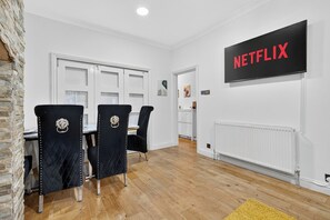 A modern room with a dining area, a wall-mounted TV displaying 'NETFLIX,' and a white door. - Ssalford Spacious 4BR House Sleeps 7 + Garden (Greater Manchester)