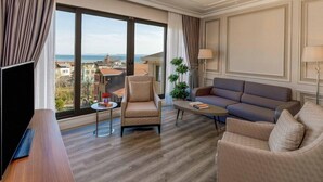 Habitación de hotel con un ventanal grande, un sofá, una silla, una mesita y un televisor.