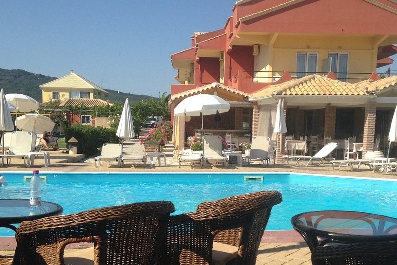 A poolside area with lounge chairs, umbrellas, and a building with a red roof.
