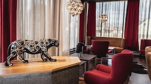 Et moderne interiør med en træreception, røde polstrede stole og en dekorativ dyreskulptur.