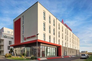 Ein modernes Hotelgebäude mit einer glatten Fassade, großen Fenstern und einer markanten Farbgebung in Rot und Weiß.