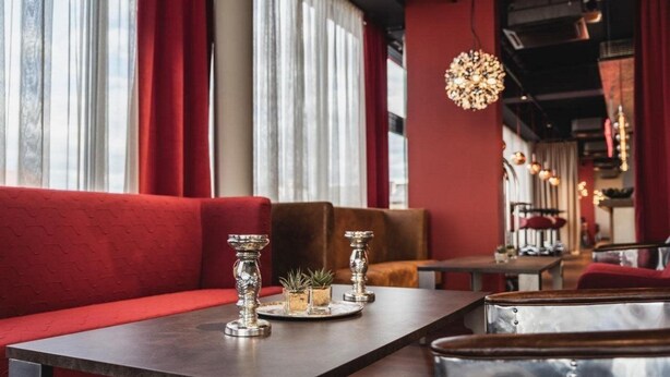 A restaurant interior with red upholstered seating, a long table with silver candle holders, and a chandelier. - Amedia Airport Graz (Feldkirchen bei Graz)