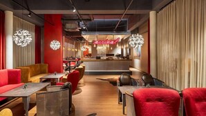 A modern interior with a reception desk, red and yellow seating, and pendant lighting. - Amedia Airport Graz (Feldkirchen bei Graz)