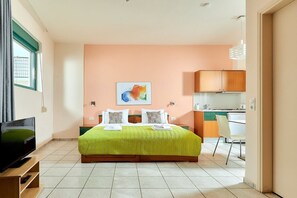 A bedroom with a bed, a television, a painting, and a kitchenette. - Bella Vista Hotel Apartments (Hersonissos)