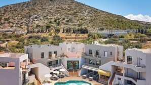 Un hotel de varios pisos con piscina, mesas al aire libre y montañas al fondo.