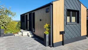 Un bâtiment moderne avec une façade en bois et en noir, une fenêtre et un petit jardin agrémenté de marches menant à l’entrée.