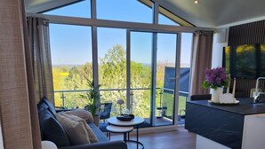 Un salon moderne comprenant un canapé, une table basse et un coin repas doté d’un plan de travail noir. De grandes fenêtres offrent une vue sur l’extérieur.
