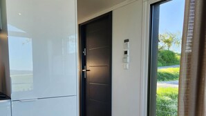 Une cuisine moderne avec des meubles blancs, une porte sombre et une porte-fenêtre coulissante donnant sur un espace extérieur.