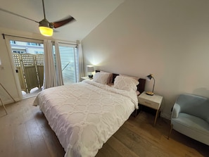 Ein Schlafzimmer mit einem Bett, zwei Nachttischen, einem Deckenventilator und Blick ins Freie.