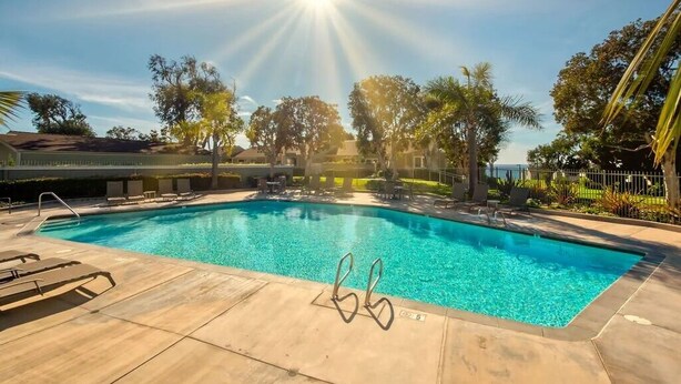 Una piscina con raggi di sole, lettini e alberi.