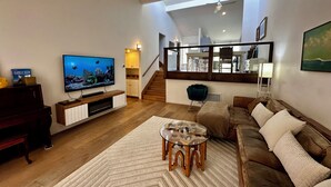 Un soggiorno con televisore, divano, tavolino e vista su cucina e scala.