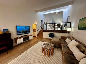Ein Wohnzimmer mit Fernseher, Sofa, Couchtisch und Blick auf eine Küche sowie eine Treppe.
