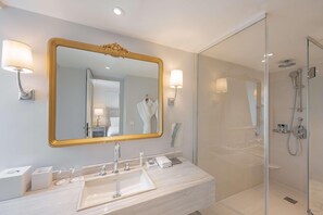 A modern bathroom with a large mirror, a sink, and a glass-enclosed shower. - Hotel Du Louvre (Paris)