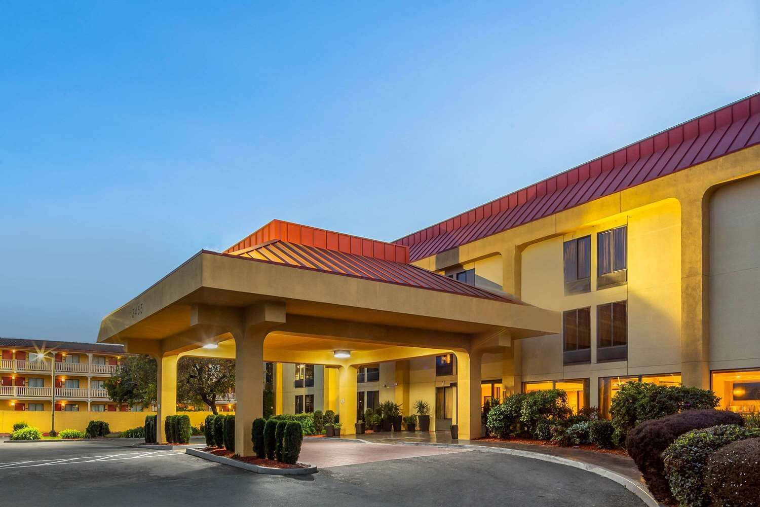A hotel with a covered entrance, multiple floors, and a red roof.