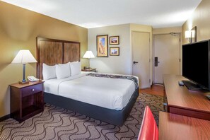 A hotel room with a bed, two bedside lamps, a TV, a desk, and a door. - LA Quinta INN AND Suites BY Wyndham Oakland Airport Coliseum (Oakland)
