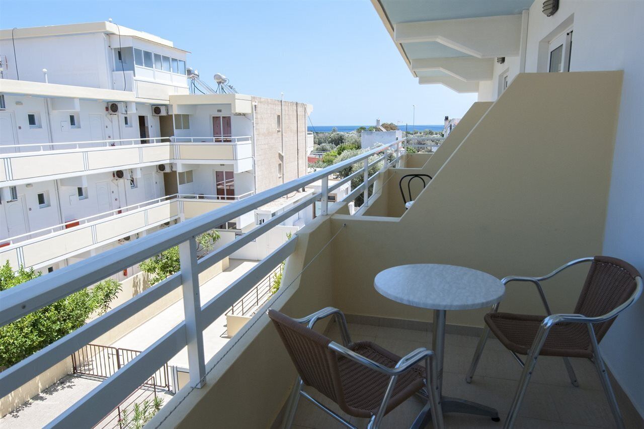 En balkon med bord og stole, der giver udsigt over et boligområde og havet.
