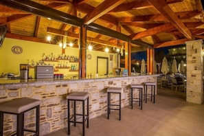 A bar area with stone walls, wooden beams, and bar stools. - Georgia Afandou Hotel (Rhodes)
